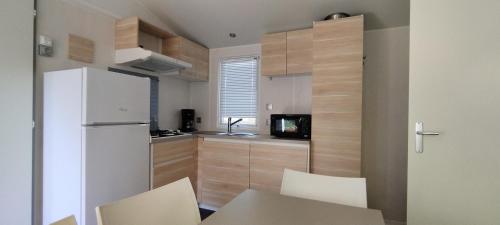 La cuisine est équipée d'un réfrigérateur blanc et de placards en bois. dans l'établissement Camping Parc des 7 Fonts, à Agde