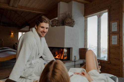 a man in a robe talking to a woman in front of a fireplace at Natur- und Wellnesshotel Höflehner in Haus im Ennstal