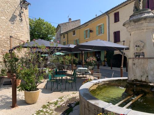 une fontaine dans une cour avec des tables et des parasols dans l'établissement Hôtel Restaurant L’Observatoire, à Saint-Michel-lʼObservatoire