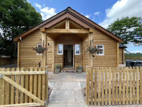 una cabaña de madera con una valla delante en The Haystack Lodge, en Tarporley