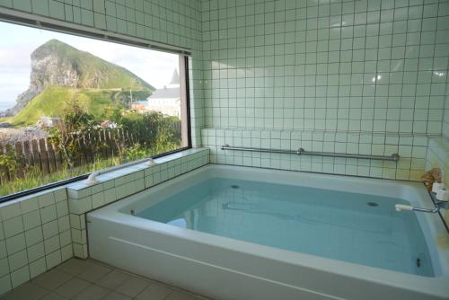 a bath tub in a tiled bathroom with a window at Shimanoyado Kamuirishiri in Rishirifuji