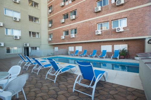 a swimming pool with blue chairs and a building at Hotel Royal in Colonia del Sacramento