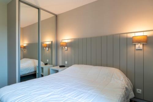 a bedroom with a large white bed and a mirror at Les Thermes 515 - Appt avec piscine partagée in Concarneau