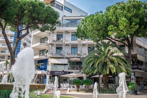a building with trees in front of a fountain at Monaco Suites Hotel in Lignano Sabbiadoro