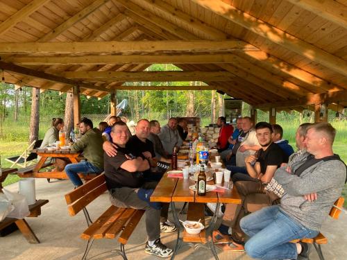 un grupo de personas sentadas en mesas en un pabellón en Leśne zacisze-pole namiotowe, en Pisklaki