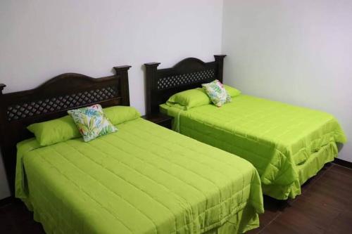 2 camas con sábanas verdes en una habitación en Casa Elohim, en Iztapa