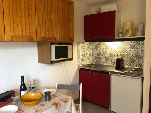 une cuisine avec des placards rouges et une table avec un four micro-ondes dans l'établissement Charmant studio rénové aux Molanès - Balcon, parking privé, proche télécabine et navette - FR-1-165A-177, à Uvernet