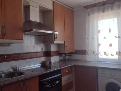 a kitchen with wooden cabinets and a sink and a window at Apartamento playa de los Lances in Tarifa