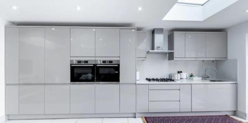 a white kitchen with white cabinets and appliances at Spacious and Comfy 6BD House - Ilford! in Ilford