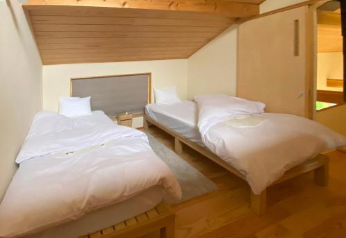 two beds in a room with white sheets at Garni MonyaMonya/ガルニモニャモニャ in Hokuto