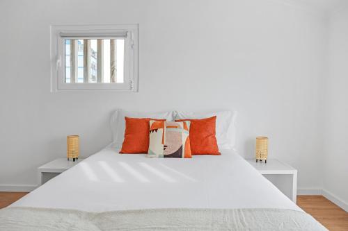 a white bed with orange pillows and a window at One bedroom Apt in Almada with River view! in Almada
