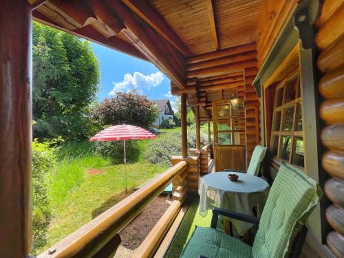 un porche de una cabaña de madera con sombrilla y mesa en Chalet Birdieferienhaus by Interhome, en Leisel