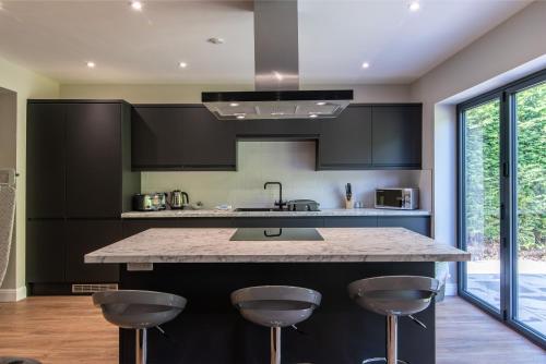 a kitchen with black cabinets and a island with bar stools at Bagworth House - Spacious 4BR Bungalow in Leicestershire 