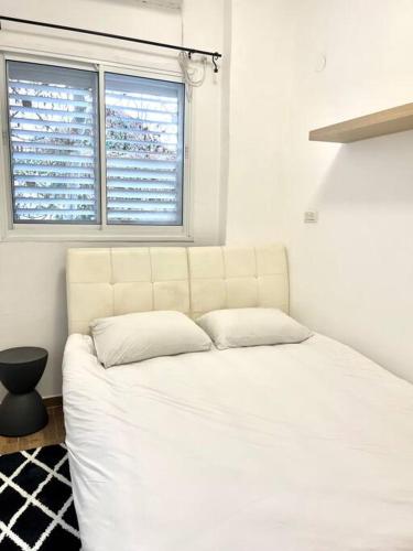 een wit bed in een kamer met een raam bij Bat Galim BEACH apartment in Haifa