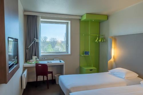 ノジャン・シュル・マルヌにあるカンパニール ノジャン シュル マルヌのベッド2台、デスク、窓が備わるホテルルームです。