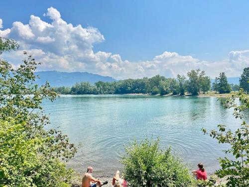 a group of people sitting on the shore of a lake at Seeparkvilla – Wohlfühlen am See und im Grünen in Bregenz