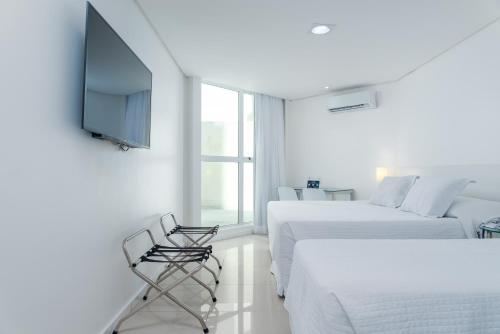 a white room with two beds and a flat screen tv at Hotel Brisa Praia Pajuçara in Maceió