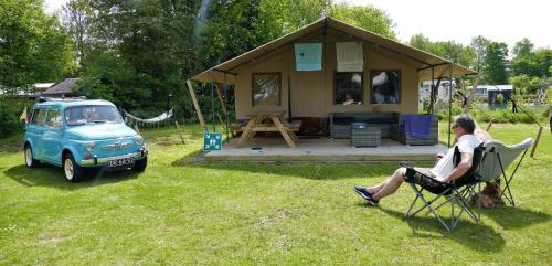 a woman sitting in a chair in front of a small house at Safaritent Sarek, Wolvenspoor 10 in Vledder
