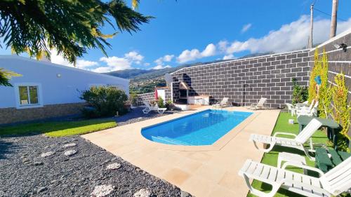 a backyard with a swimming pool and chairs and a house at Loreto Rose, Panoramic Ocean and Mountain View in Arco da Calheta