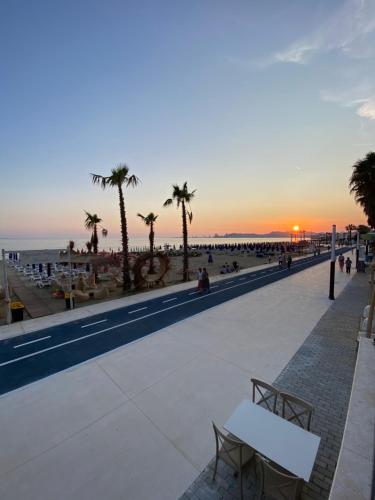 a sunset over a beach with palm trees and a white bench at Xhani's Rooms in Durrës