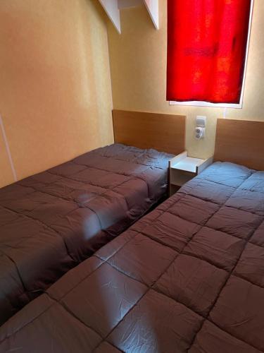 - 2 lits dans une chambre dotée d'une fenêtre rouge dans l'établissement Mobil-home au bord de l’eau, à Feins