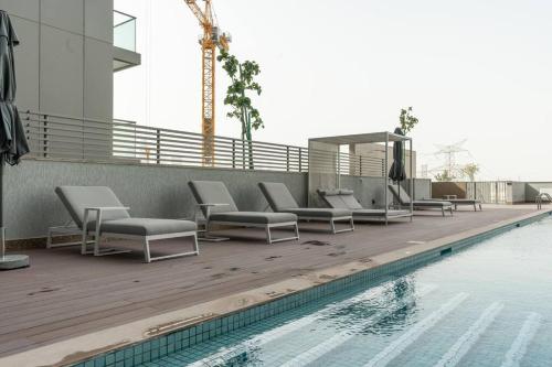 a swimming pool with lounge chairs next to a building at Modern 1bdr - 10min from Burj Khalifa - Sobha Waves in Dubai