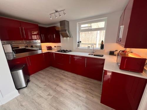 eine Küche mit roten Schränken, einem Waschbecken und einem Fenster in der Unterkunft Golf Open Property to Rent Dates available 15th - 23th July in Wallasey