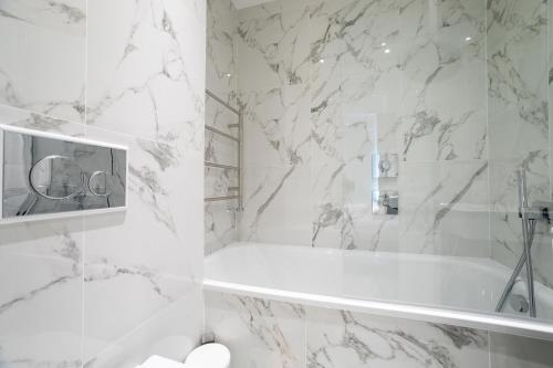La salle de bains blanche est pourvue d'une baignoire et de murs en marbre. dans l'établissement The Hearth of Westminster, à Londres