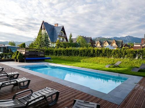 a swimming pool with chairs and a house at Hotel Paryski Art & Business Zakopane - Basen Jacuzzi Sauna Małpi Gaj in Zakopane