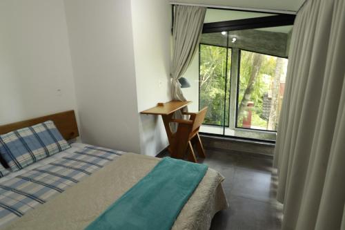 a bedroom with a bed and a desk and a window at Casas Temporada Aldeia Niura Opy in Florianópolis