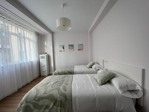 a white bedroom with two beds and a window at Cedemar 2 in Cedeira