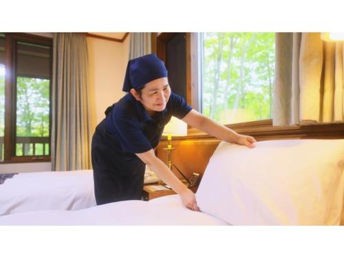青森市にあるSukayu Onsen Hakkoda Hotel - Vacation STAY 66849vの女性がホテルの部屋でベッドを作る