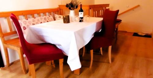 APARTMENT CHALET -BOHINJ- Pokljuka- Triglav National Park في Koprivnik v Bohinju: طاولة بيضاء مع كراسي حمراء وزجاجة نبيذ
