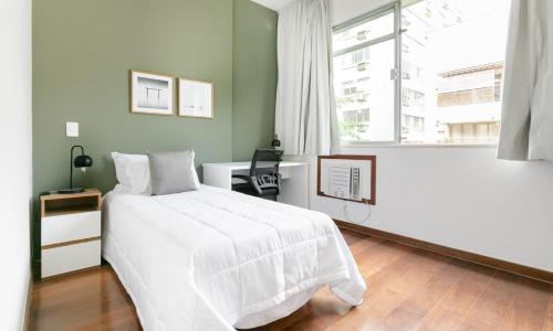 1 dormitorio con cama blanca, escritorio y ventana en Tabas - Lindíssimo apê 3 quartos na Lagoa - LG0006, en Río de Janeiro