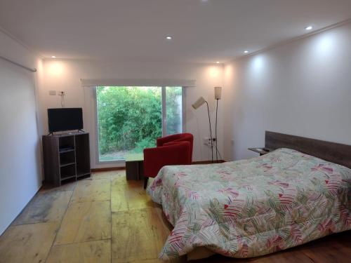 ein Schlafzimmer mit einem Bett, einem Fenster und einem roten Stuhl in der Unterkunft El parquecito in Tandil