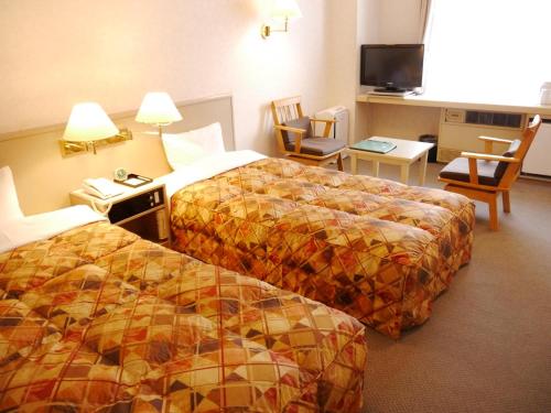 a hotel room with two beds and a flat screen tv at Biei Shirogane Onsen Hotel Park Hills in Biei