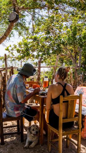 a man and a woman sitting at a table with a dog at Tatajuba Hostel Casa Pascual in Tatajuba
