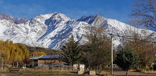 a snow covered mountain in the distance with a building and trees at Cerro Indio in Potrerillos