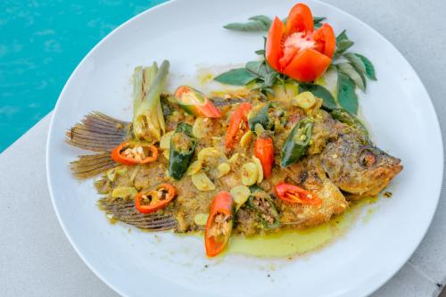 a white plate of food with a fish and vegetables at The Dukuh Retreat in Tabanan