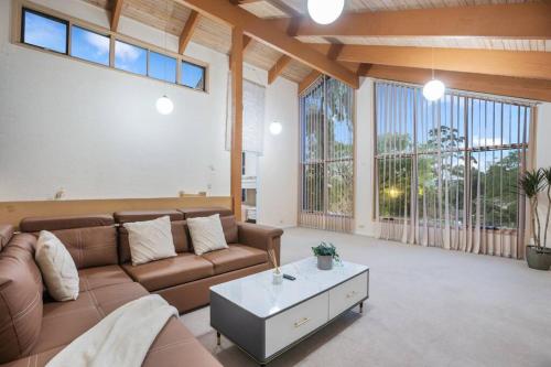 a living room with a brown couch and large windows at Stylish Retreat Family House 5BRM Wheelers Hill in Wheelers Hill