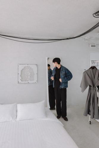 a man standing in a white room next to a bed at Art Mai Gallery Nimman Hotel Chiang Mai in Chiang Mai