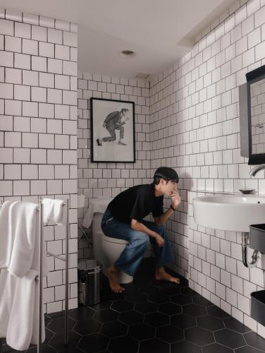 a man sitting on a toilet in a bathroom at Art Mai Gallery Nimman Hotel Chiang Mai in Chiang Mai