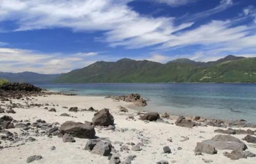 a beach with rocks and the ocean and mountains at Parque suizo, Pucon in Pucón