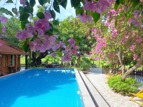 a swimming pool surrounded by trees and pink flowers at Tam Coc Sunshine Homestay in Ninh Binh