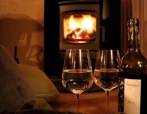 two wine glasses and a bottle on a table in front of a fireplace at Serenity Gully 