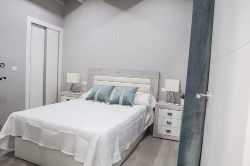 Dormitorio blanco con cama blanca y almohadas azules en Elegante y acogedor. Buena ubicación, en Osuna