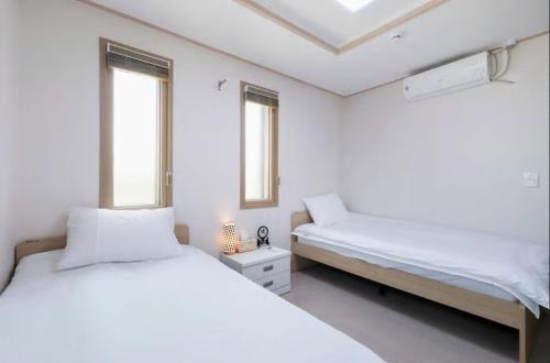 two beds in a white room with two windows at Hub Guest House in Incheon