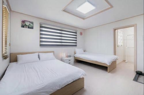 a white bedroom with two beds and a window at Hub Guest House in Incheon
