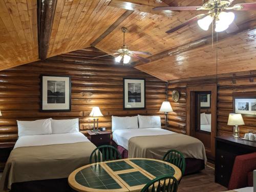 two beds in a room with wooden walls and a table at Teton Court Motel in Pinedale