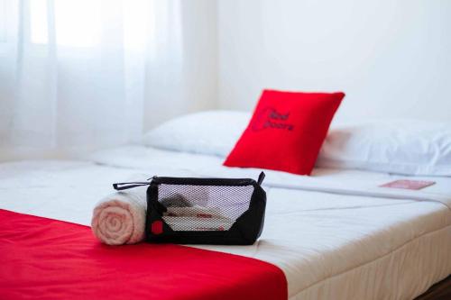 a bed with a red pillow and a bag on it at RedDoorz at Damar Mas Gunung Kelud Kediri in Kediri